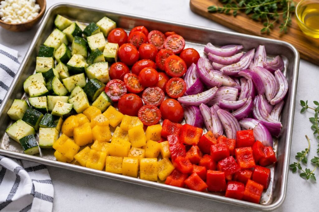 chopped zucchini, cherry tomatoes, red onion, yellow squash and red bell pepper on a sheet pan